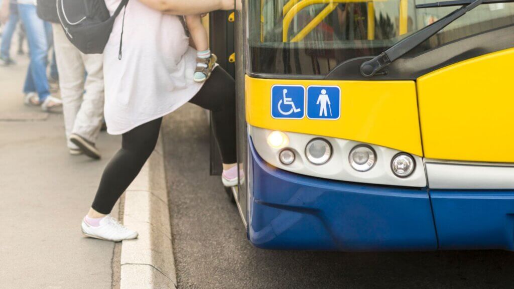 Front of an HSR bus with accessibility and seniors symbols. A pregnant passenger carrying a toddler and a backpack is boarding the bus.